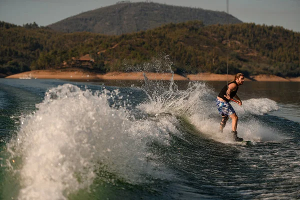 Su sıçratan nehir dalgası ve elinde ip tutan ve sörf tahtasında gezen adamın manzarası harika..