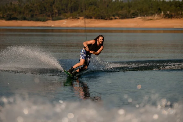 Atletik sakallı adam ipi tutuyor ve ustalıkla nehirde wakeboard sürüyor..