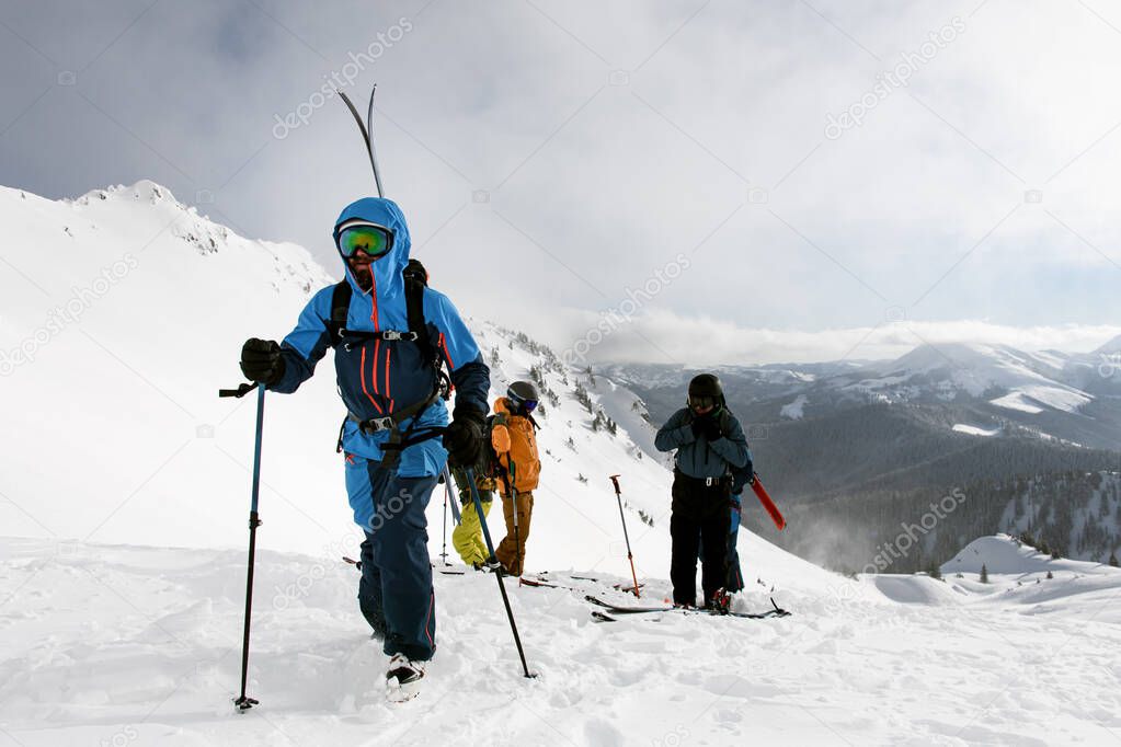 group of active people are climbing snowy hill on mountain on skis and splitboards at sunny winter day. Winter activities, ski touring