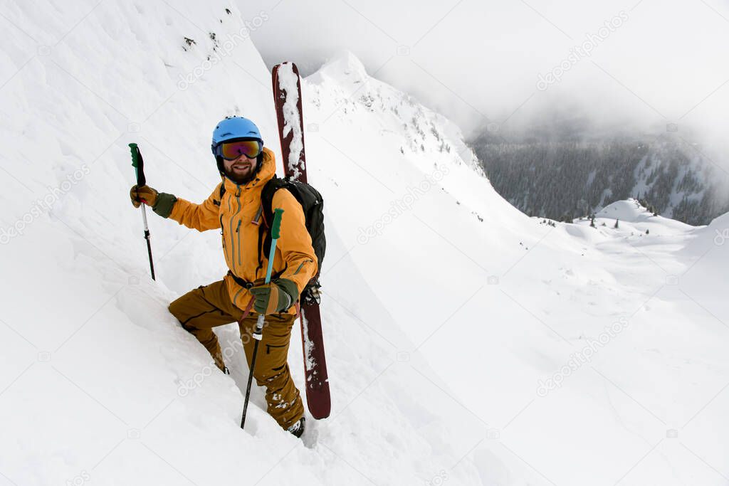 happy male skier with skitour equipment and splitboard is climbing the snowy hill. Ski touring in mountains.