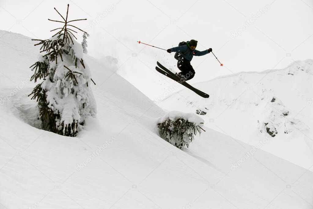 Beautiful view of active skier skilfully jumping over slopes of snow-capped mountains. Snow and winter activities, ski touring.