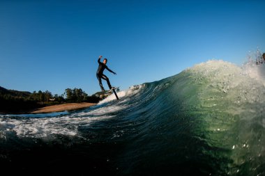 Siyah dalgıç kıyafetli genç atletik bir adam folyoyla dalgadan aşağı iniyor. Su sporları etkinliği.