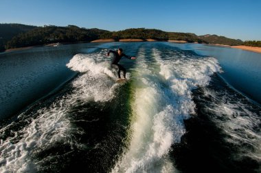 Siyah dalgıç kıyafetli atletik bir adamın yüksek açılı görüntüsü dalgada sörf tahtasıyla ustaca zıplıyor.
