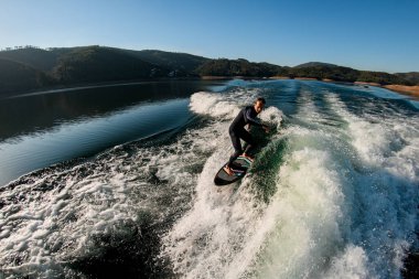 Siyah dalgıç kıyafetli atletik bir adamın güzel manzarası. Dalgalanan dalgalarda sörf tahtasıyla ustaca sürüyor.