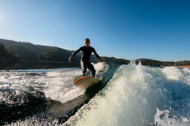 Aktif erkek, mavi gökyüzü arka planında dalgalanan dalgada siyah bir dalgıç kıyafetiyle aşağı iniyor.