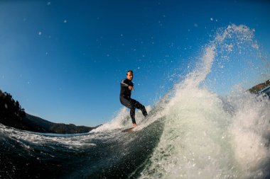 Su sıçratan dalganın güzel manzarası siyah dalgıç kıyafetli genç bir adamın wakesurf tahtasına bindiği