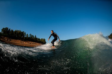 Siyah dalgıç kıyafetli genç atletik bir adam uyanma tahtasında dengede duruyor.