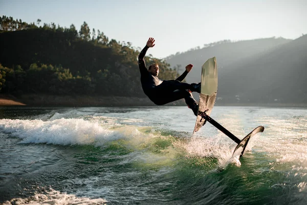 波から落ちてくる箔板の黒いウェットスーツの男の壮大な景色 — ストック写真