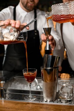 Çelik bardaklara yakın çekim ve barın tezgahına şarap bardağı. Barmen bardağa su döker.