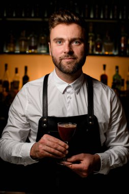 Yakışıklı erkek barmen bulanık bar arka planında kristal şarap bardağında nefis bir alkollü kokteyl servisi yapıyor.