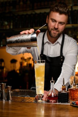 Erkek barmen ustalıkla çelik bardaktan şeffaf cam bardağa lezzetli bir kokteyl doldurur. Tezgahtaki bar ekipmanlarının çeşitliliği