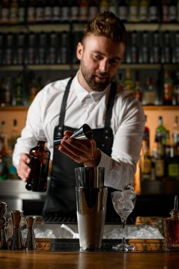 Barın tezgahındaki çelik bardakların manzarasında barmen dikkatle bir zencefilden su doldurur. Yakınlarda buz küpleri olan bir bardak.