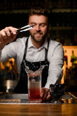 Barmenlerin maşadan bir parça buz attığı barın tezgahına su sıçratan şeffaf cam manzarası harika. Arkadaki barmen.