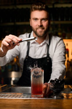 Şeffaf cam manzarası barın tezgahına su sıçratarak barmenlerin maşadan bir parça buz attığı yer. Arkadaki barmen.