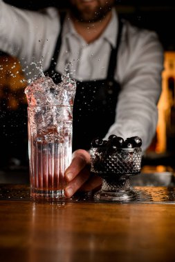 Su sıçratan bir bardağın ve tezgahında böğürtlen olan kristal bir tabağın harika manzarası. Arkadaki barmen.