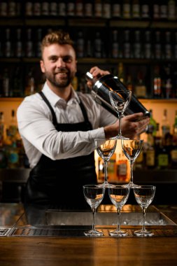 Bardaki boş şampanya bardaklarından yapılmış güzel bir kule ve arka planda titreyen bir erkek barmen.