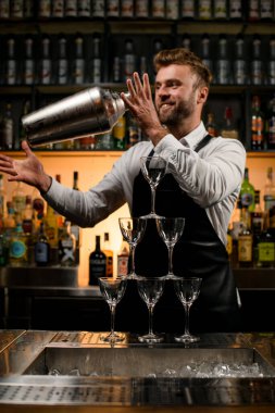Bar tezgahında boş şampanya bardaklarından yapılmış muhteşem bir kule ve arka planda titreyen bir erkek barmen.