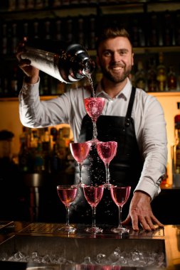 Barmenin büyük bir bardaktan lezzetli bir kokteyl döktüğü bardaktan yapılmış kulenin yakın görüntüsü.