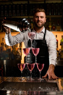 Barmenin bardaktan yapılmış harika bir kule manzarası var. Büyük bir bardaktan lezzetli bir kokteyl dolduruyor.