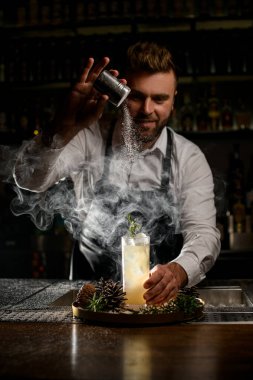 Profesyonel barmen pudra şekerle süslüyor bardakta dumanı tüten bir kokteyl var tezgahta.