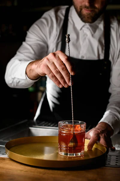 hand of a male bartender gently mixes a cocktail in a glass with a long bar spoon