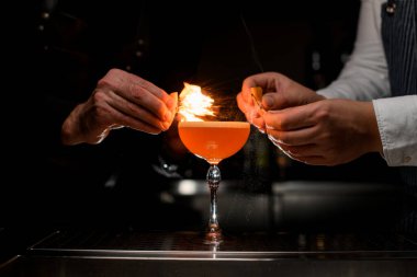 Güzel bardakların üzerine su sıçrattığı ve iki barmenin ellerini ateşe verdiği kokteyl ile yakın plan.