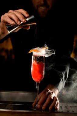 Barın tezgahında portakal kabuğuyla süslenmiş kırmızı alkollü içeceklerle dolu yüksek kadehlerin yakın çekimi.