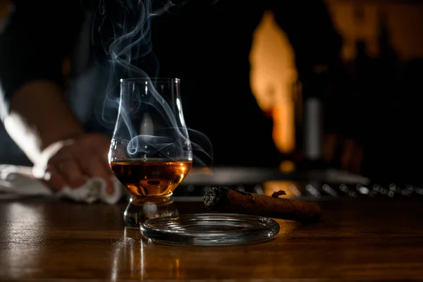 Beautiful close-up of smoking cuban cigar on ashtray and glass with whiskey on blurred background
