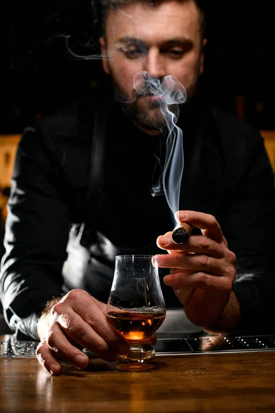 amazing view on smoking cuban cigar in the hand of a male bartender and a glass of cognac on the bar counter