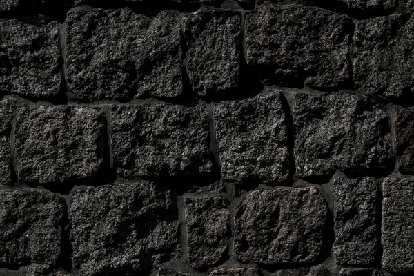 Texture of old stone wall with dark grey rocks of different shape. Part of stone wall for background or texture