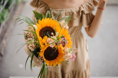 Parlak ayçiçeklerinden ve diğer çiçeklerden oluşan muhteşem bir buket ve elinde yeşil bir kadın