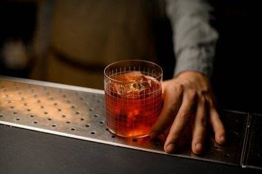 Selective focus on transparent glass with grid pattern full of cold cocktail and male hand near it. Blurred background