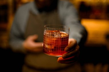 Selective focus on transparent glass with grid pattern full of cold cocktail in male hand . Blurred background
