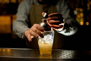 close-up of transparent shaker with liquid and ice cubes which the hand of male bartender carefully closes with a lid
