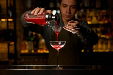 magnificent view of the wine glass into which the bartender pours cocktail from glass shaker through a sieve