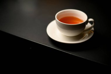 Beautiful white porcelain cup of tea and saucer on black table. Delicious breakfast concept. Close-up
