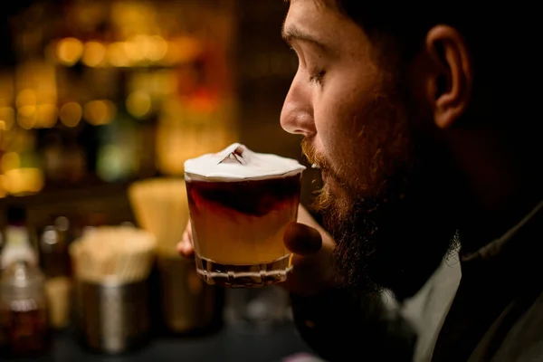 close-up side view of the face of man drinking signature alcoholic cocktail with foam. Blurred background