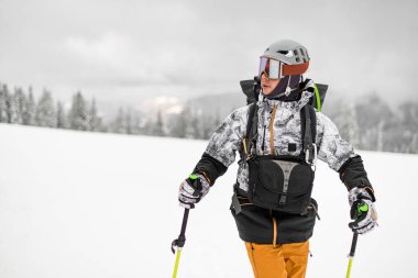 Male skier with ski suit and helmet and trekking poles on blurred winter landscape background