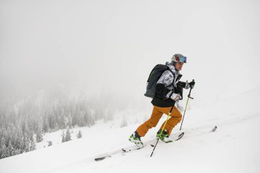 Side view of skier man with trekking poles climbing up snowy mountain slope. Active healthy lifestyle