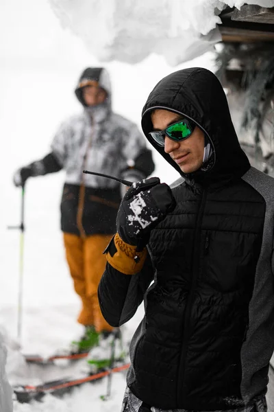 Человек Темных Очках Черной Куртке Капюшоном Голове Размытый Лыжник Заднем — стоковое фото