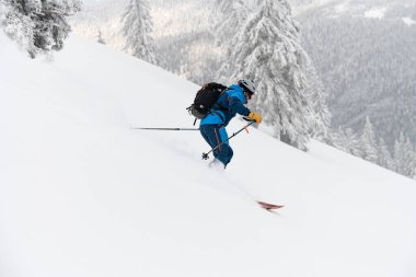 side view on skier riding on deep fresh powder snow down the slope. Freeride skiing concept