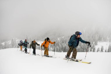 Group of male skiers hiking on skis in deep snow on cold winter day. Tourism, exploration and skitour concept.