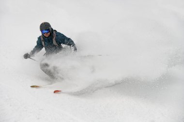 Close-up of male skier riding down on snow-covered mountain slope and splash of fresh snow around him. Freeride skiing concept