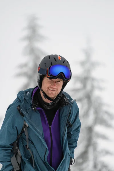 Portrait of male skier in ski helmet and mask on his head against the backdrop of blurred evergreen trees