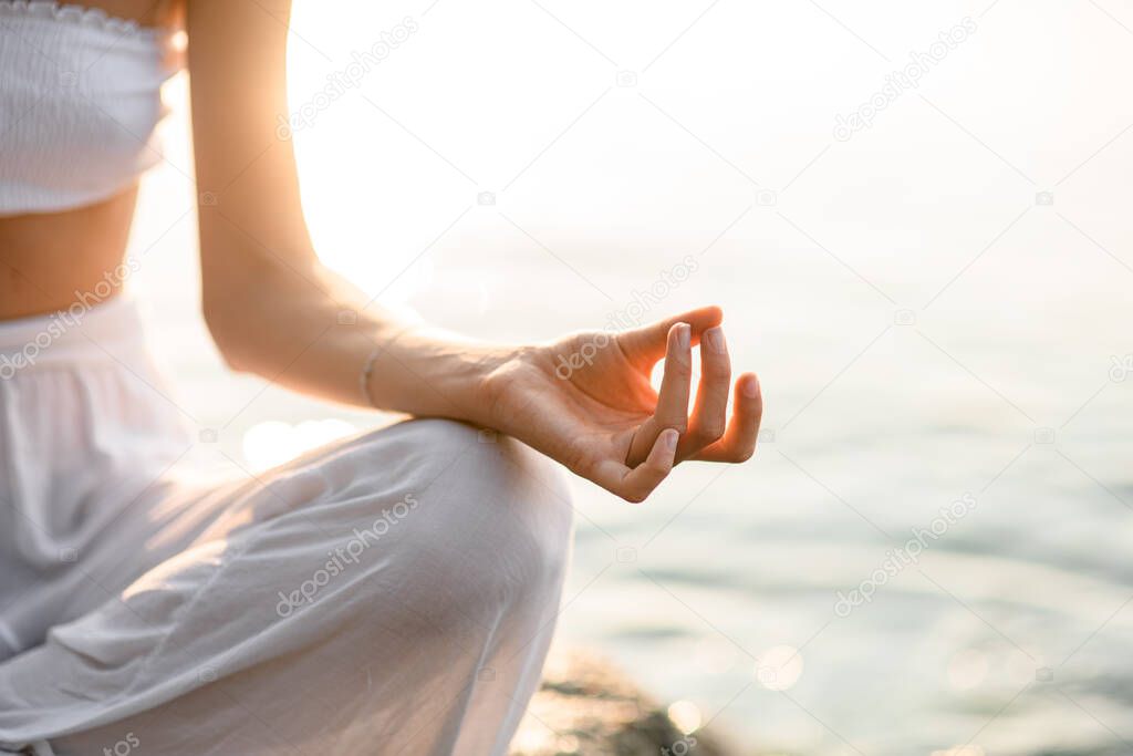 Close-up hand of caucasian woman meditating in lotus pose on the beach. Photo fragment. Selective focus on hand