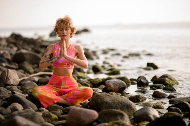 Beautiful woman practicing yoga sitting pose folded hands. Prayer position yoga outdoor on coast. Relaxation yoga exercise concept.