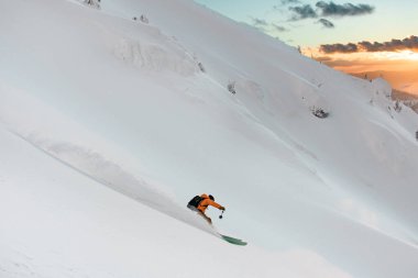 Side view of male freerider skier speedly riding down on snow-covered mountain slope and splashing snow around him.
