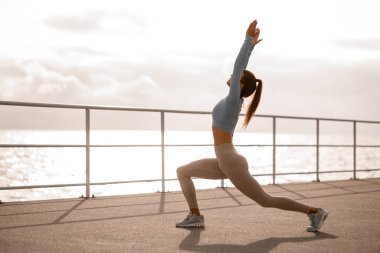 Sportif bir kadının hamlelerle antrenmandan önce esneme egzersizleri yapması. Aktif spor yaşam tarzı konsepti. Açık havada eğitim, sağlıklı yaşam tarzı konsepti.