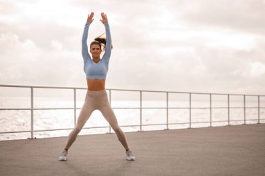 Deri taytlı ve üstü açık kadınlar antrenmandan önce kaslarını ısıtır ve kollarını açarak egzersiz yapar.