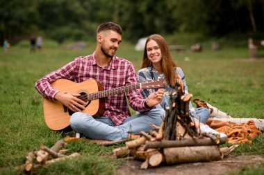 Parkta gitar çalan gülümseyen genç bir çift. Romantik atmosfer. Aşk hikayesi. Piknikte aşık mutlu çift.
